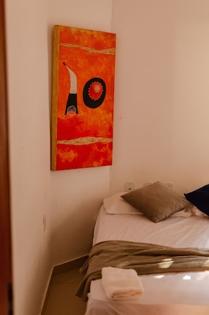 Ein Zimmer mit einem Bett, einem Kissen und einem an der Wand hängenden Kunstwerk.