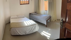 Une chambre avec deux lits, l’un recouvert d’une simple couverture blanche et l’autre d’une couverture à motifs.