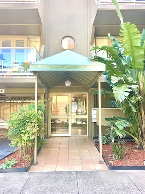Enter through the covered walkway, flanked by lush greenery, to the hotel's main entrance.