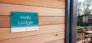 Een bordje met de tekst 'Holly Lodge' op een houten wand.