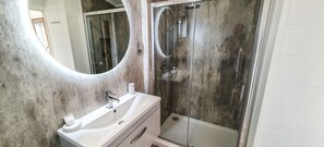 Een badkamer met een wit wastafelmeubel, een grote spiegel, een douchecabine en een bad.