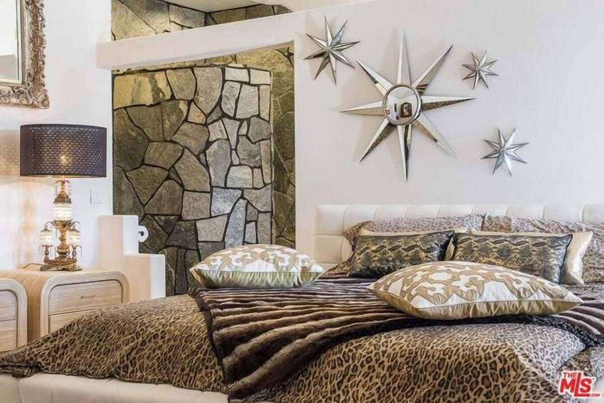 Une chambre avec un mur en pierre, un lit recouvert d’une couette à motifs léopard et une décoration murale en forme d’étoile.