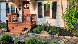 Una casa con porche delantero, banca de madera, señal indicando la Ruta del Kentucky Bourbon y un pequeño jardín con plantas y rocas.