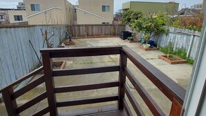 A view from a balcony with a wooden railing, a concrete floor, and a view of neighboring buildings and a garden area. - Comfy 2 bdrm 1 bath 3 beds in-law unit w/kitchen (Daly City)