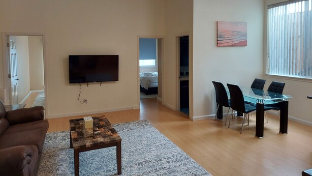 A living room with a flat-screen TV, a brown leather sofa, a coffee table, and a dining area with a glass table and chairs. - Comfy 2 bdrm 1 bath 3 beds in-law unit w/kitchen (Daly City)
