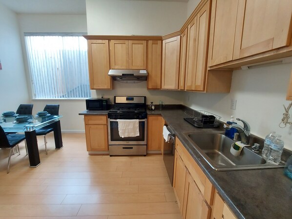 A compact kitchen with wooden cabinets, a microwave, an oven, a sink, and a dining table with chairs.