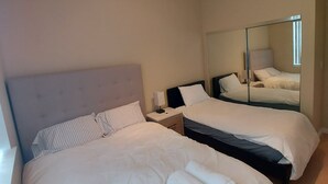A hotel room with two beds, a nightstand, a lamp, and a ceiling light fixture. - Comfy 2 bdrm 1 bath 3 beds in-law unit w/kitchen (Daly City)