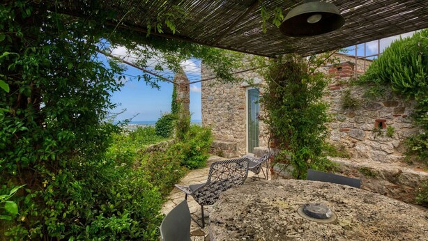 A stone pathway leading to a seating area with a view of the sea, surrounded by lush greenery and a rustic stone wall. - Castle with pool and sea views for 6 People (Monteggiori)