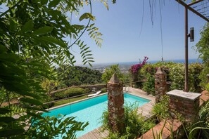 A pool with a view of the city in the background, surrounded by greenery and stone structures. - Castle with pool and sea views for 6 People (Monteggiori)