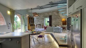 A modern kitchen with a stone wall, a dining area with a table and chairs, and a living room with a sofa and a lamp. - Castle with pool and sea views for 6 People (Monteggiori)