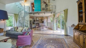 A spacious living area with a staircase leading to an upper level, a dining area, and a view through large windows. - Castle with pool and sea views for 6 People (Monteggiori)