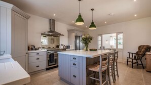 A spacious kitchen with a central island, a dining area with wooden chairs, and a large window providing natural light.