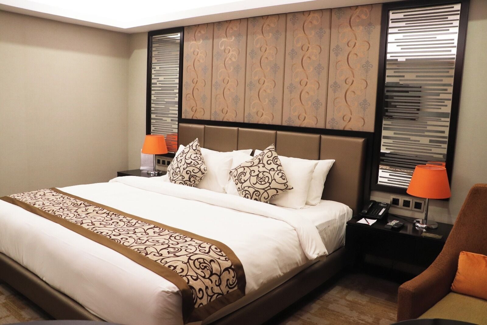 A hotel room with a large bed, two bedside tables, a chair, and a decorative headboard.