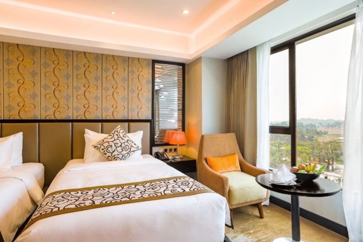 A hotel room with a large bed, a chair, a small table, and a view of the outdoors.
