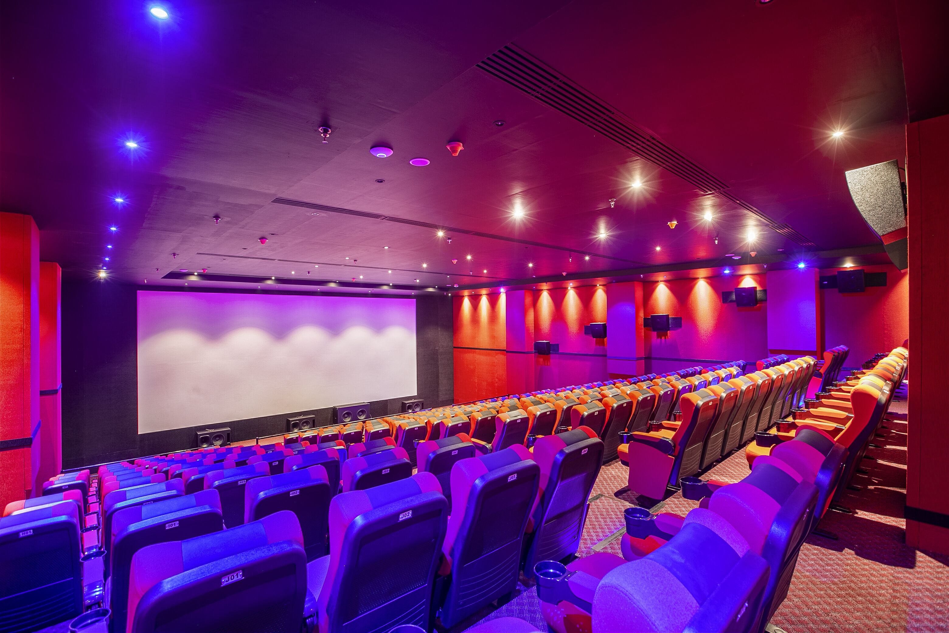 Um cinema com fileiras de assentos, uma tela grande e um esquema de cores vermelho e roxo.