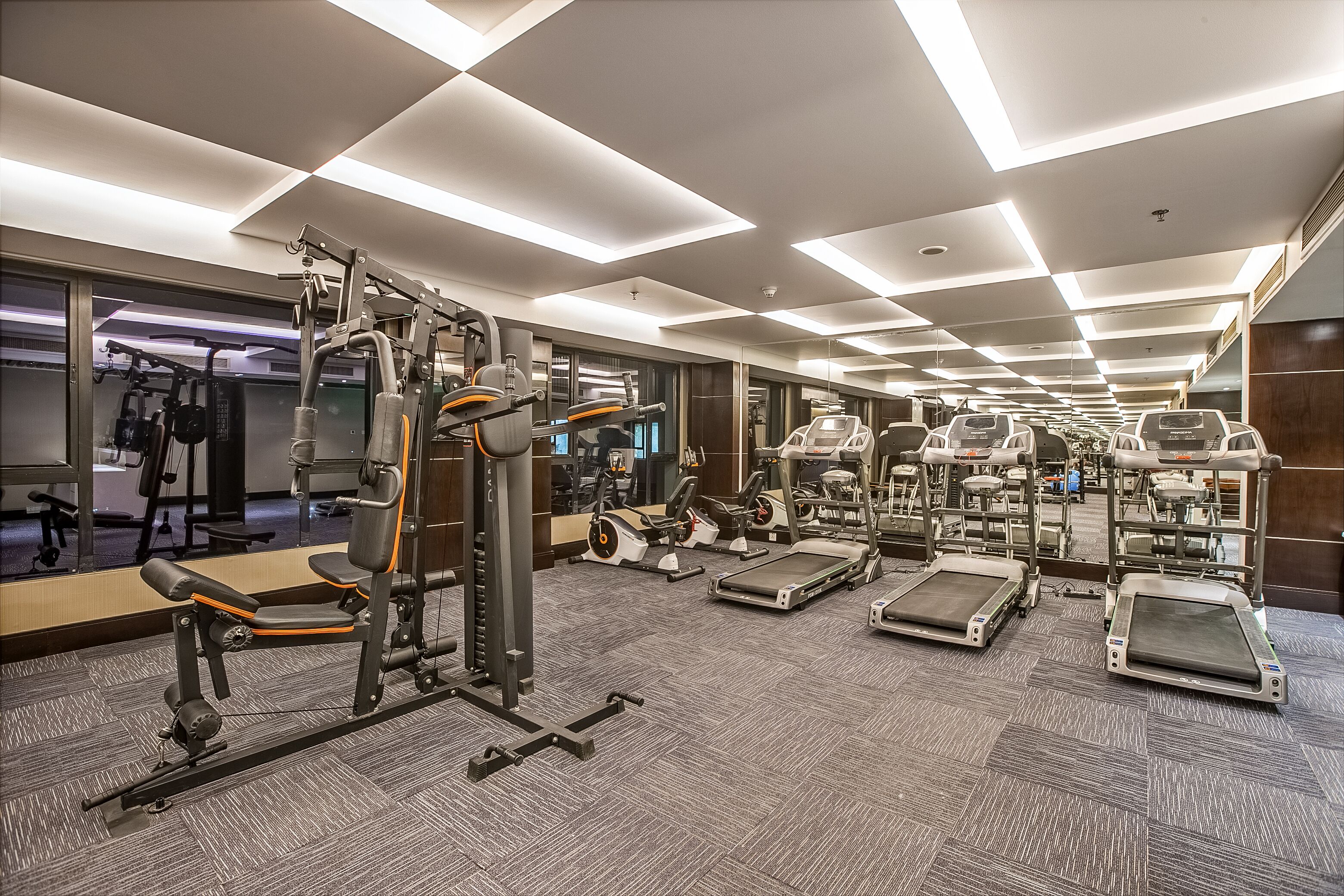 A modern gym with various exercise equipment, including treadmills and weight machines, and a large mirror reflecting the space.