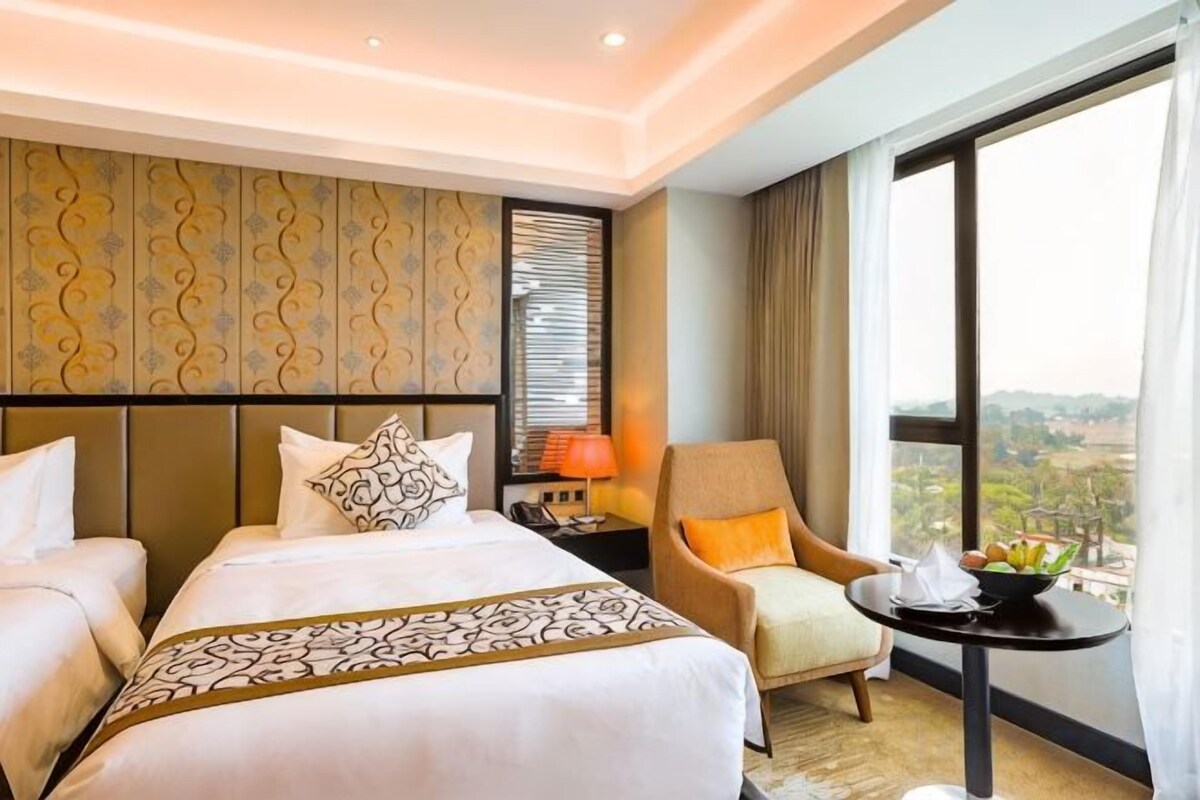 A hotel room with two beds, a sitting area with a table, and a view of the outdoors.