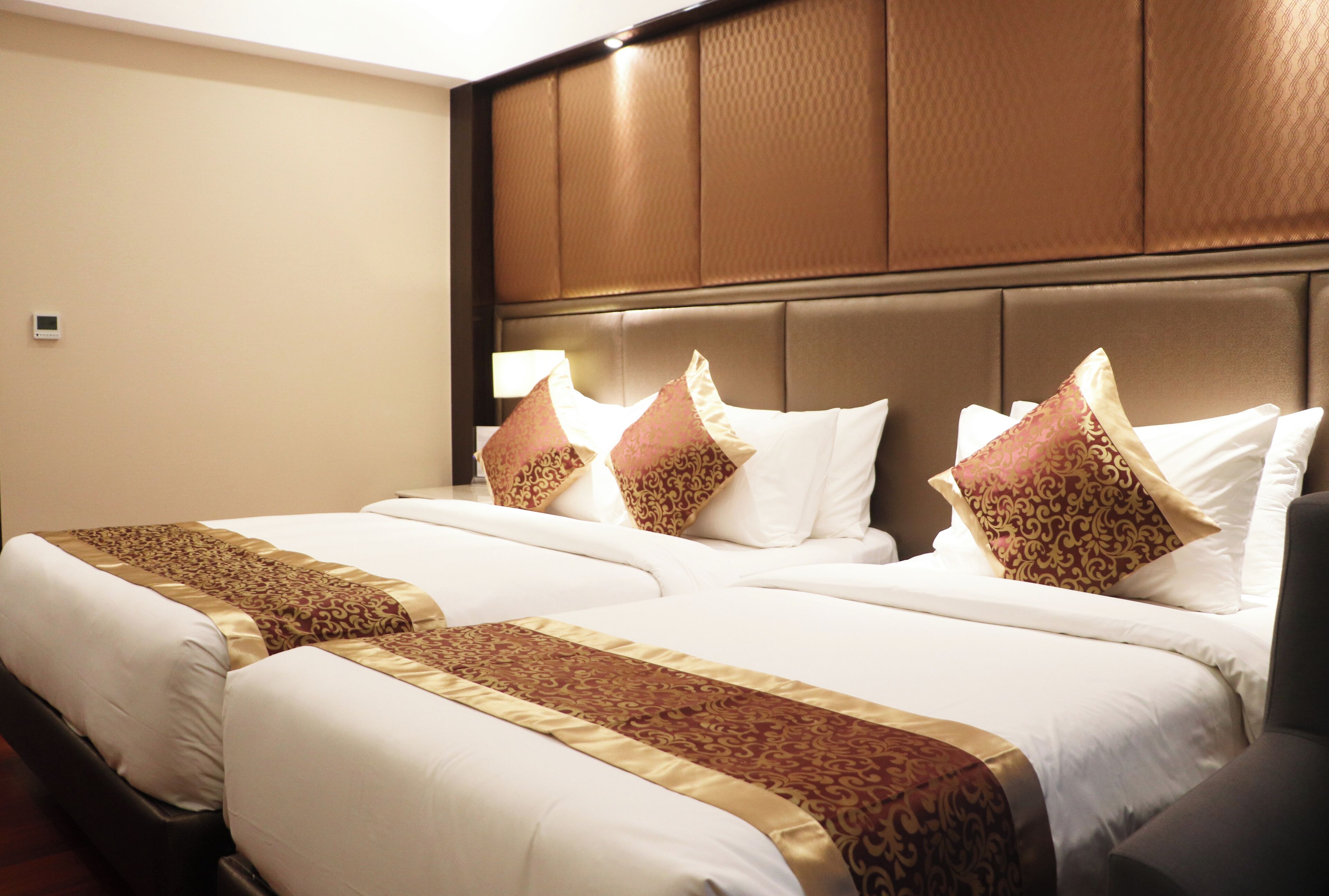 Habitación de hotel con dos camas, cada una con ropa blanca y cabeceros marrones.