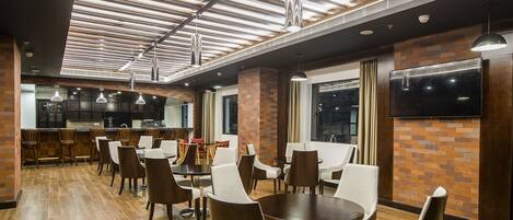 Un espace de salle à manger moderne avec un plancher en bois, des éléments décoratifs en briques et un mélange de chaises en bois et de chaises rembourrées.