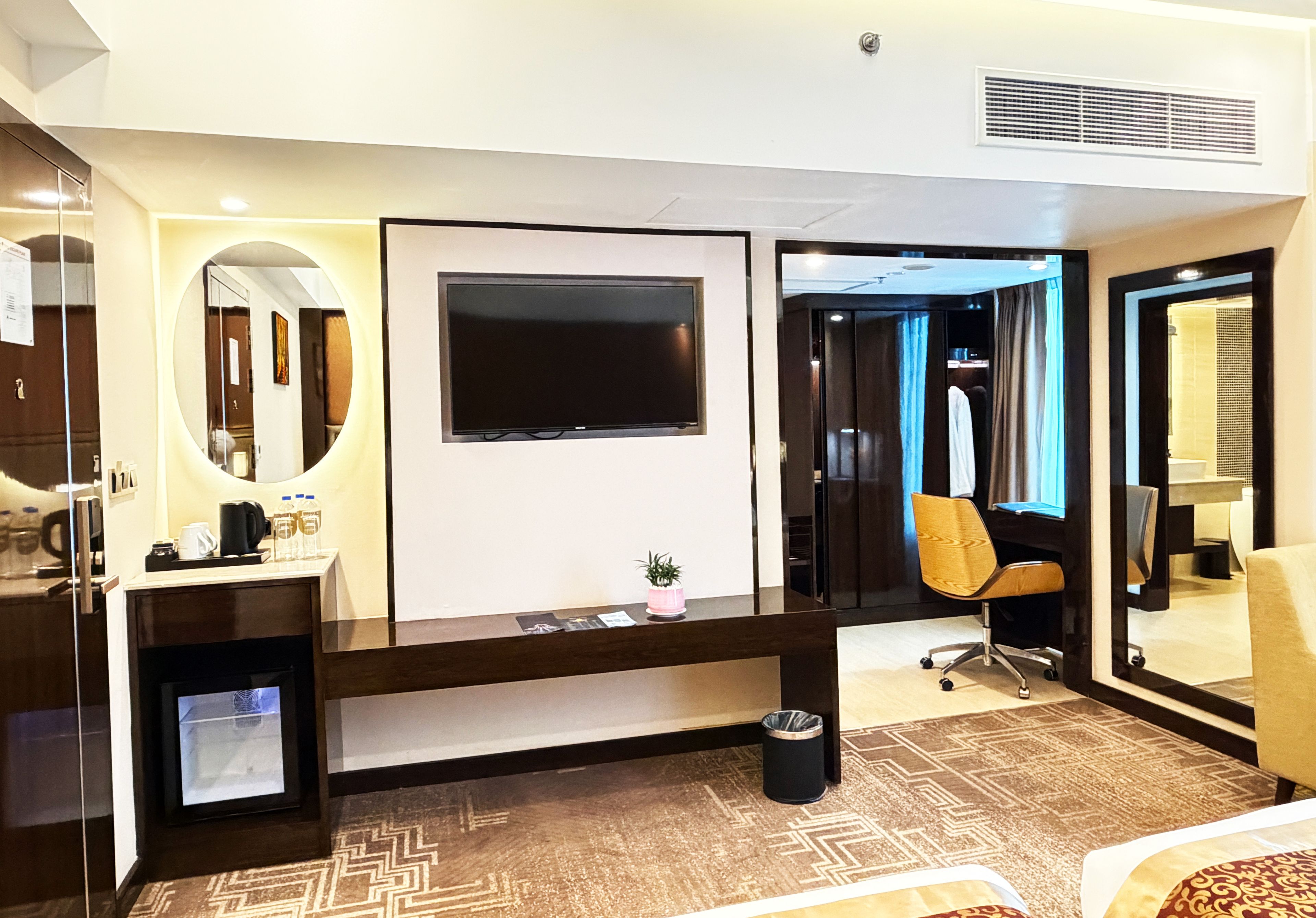 Une chambre d’hôtel équipée d’un grand téléviseur à écran plat fixé au mur, d’un bureau avec une chaise, d’une petite poubelle et d’un miroir.