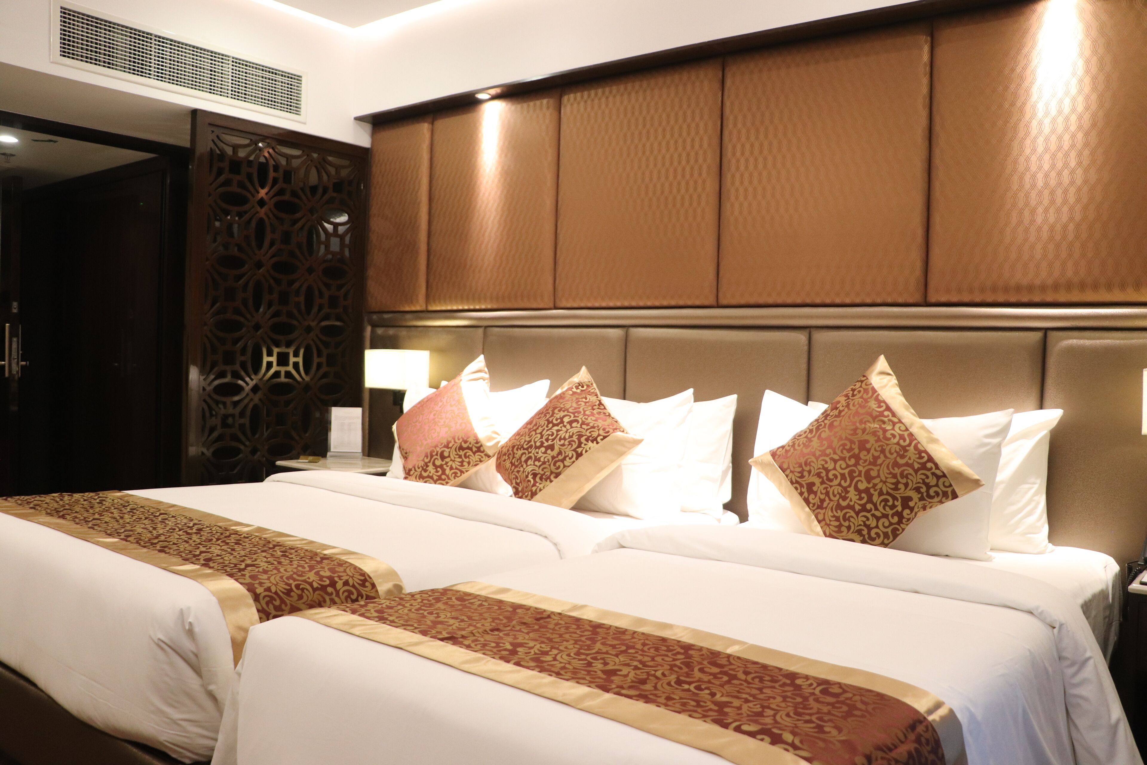 A hotel room with two beds, a large wooden headboard, and a decorative wall panel.