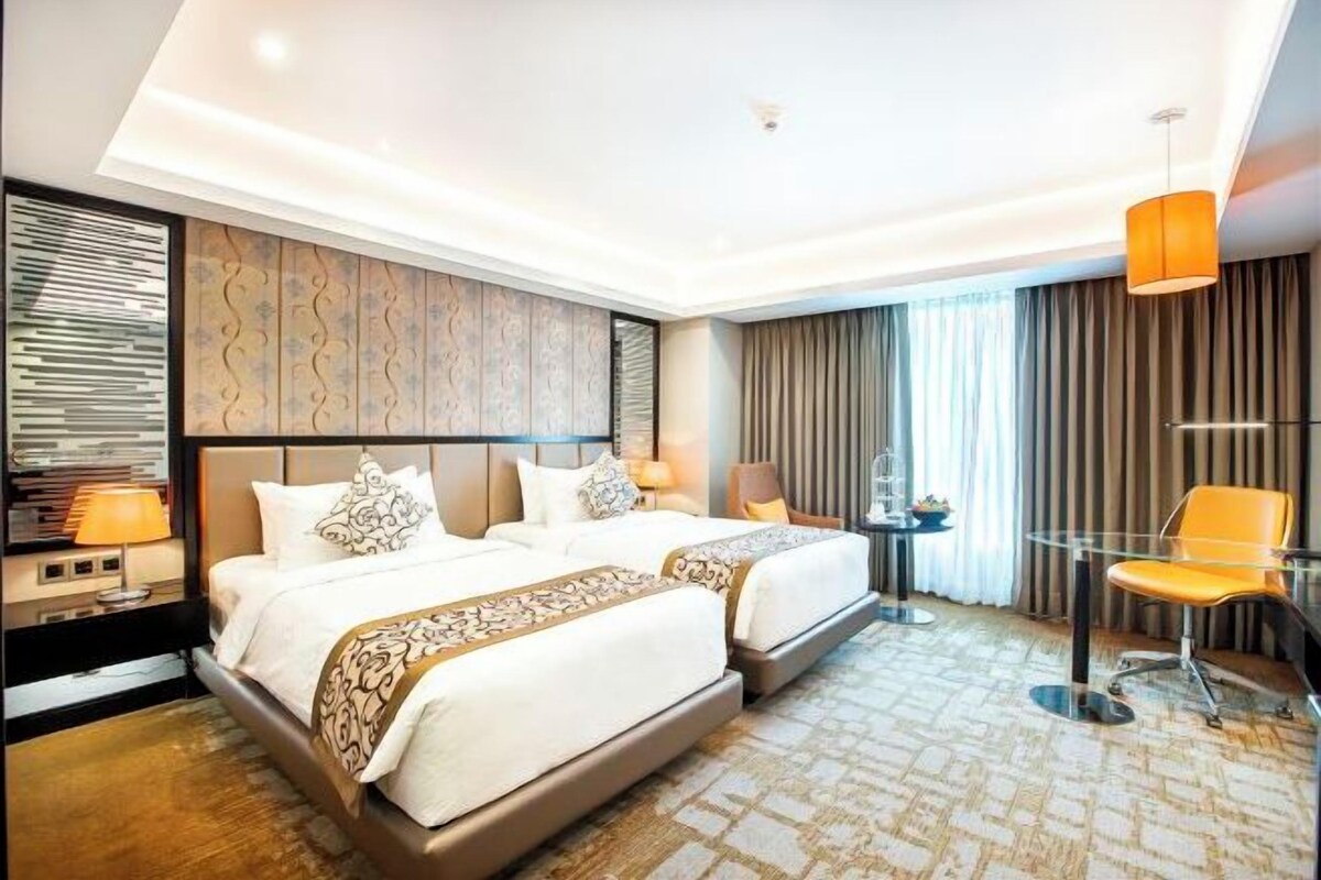 A hotel room with a large bed, a desk, a chair, and a view of the city.