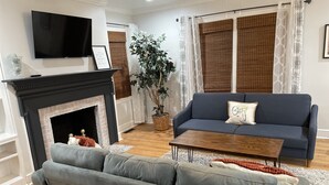 Un salon avec une cheminée, un canapé bleu, une table basse en bois et un téléviseur fixé au mur.