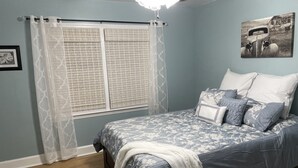 Une chambre à coucher avec un lit, des rideaux, un ventilateur de plafond et un tableau accroché au mur.