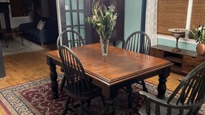 Un coin repas avec une table en bois, quatre chaises, un vase de fleurs et un tapis à motifs.