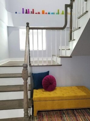 Staircase features a tufted bench with a cushion and a shelf with decorative bottles.