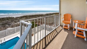 Ein Balkon mit Blick auf den Strand, ein Schwimmbad und zwei Adirondack-Stühle.