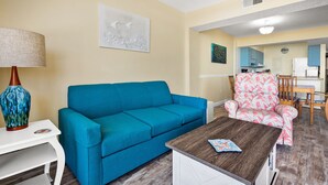 Ein Wohnzimmer mit einem blauen Sofa, einem pinkfarbenen Stuhl mit Muster, einem Holztisch als Couchtisch und einem weißen Nachttisch mit Lampe.