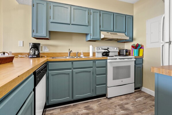 A kitchen with teal cabinets, a white stove, and a wooden countertop.
