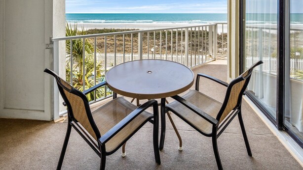Ein Balkon mit rundem Tisch und zwei Stühlen mit Blick auf Strand und Meer.