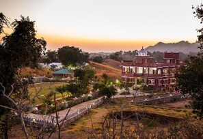 A large, multi-story building with a central dome, surrounded by a landscaped garden and a stone wall. - The Sky Imperial Kumbhalmer Resort (Kumbhalgarh)