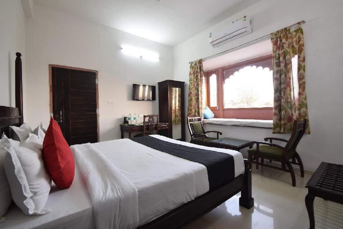 Una habitación de hotel con cama, escritorio, silla, televisor y aire acondicionado.