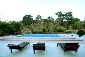 A swimming pool with lounge chairs and a stone wall in the background. - The Sky Imperial Kumbhalmer Resort (Kumbhalgarh)