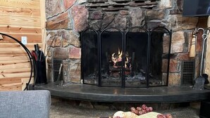 A stone fireplace with a fire, a wooden table with a charcuterie board, and a gray sofa.