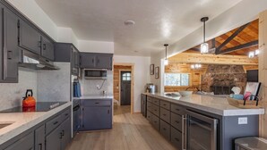 A modern kitchen with dark cabinets, a central island, and a stone fireplace.