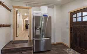 Une cuisine moderne avec un réfrigérateur en acier inoxydable, un plancher en bois et une porte en bois foncé.