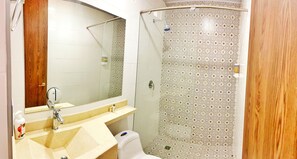 A bathroom with a beige sink, a mirror, a toilet, and a shower with patterned tiles. - Hotel Entre Lomas (Dosquebradas)