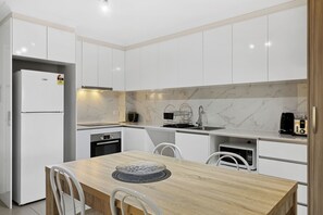 A modern kitchen with white cabinets, a wooden dining table, and white chairs.