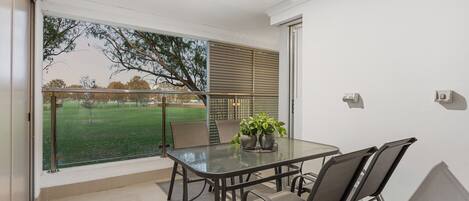 A balcony with a glass table, chairs, and potted plants.