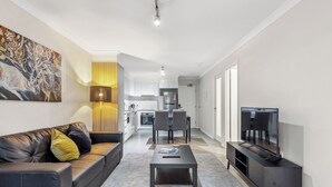 Una sala moderna con sofá, mesa de centro y mueble para la televisión. Se aprecia un comedor con sillas y mesa al fondo.