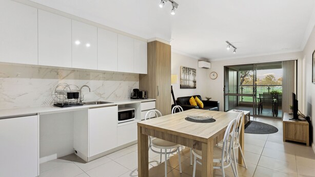 Una cocina moderna con armarios blancos, una mesa de comedor de madera y vistas al exterior.