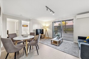 A modern living room with a dining area, a TV, and a balcony with a view. - Yaran Suites (Rockingham)