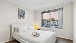 Un dormitorio moderno con una cama grande, una ventana que ofrece vistas a edificios y un cuadro en la pared.
