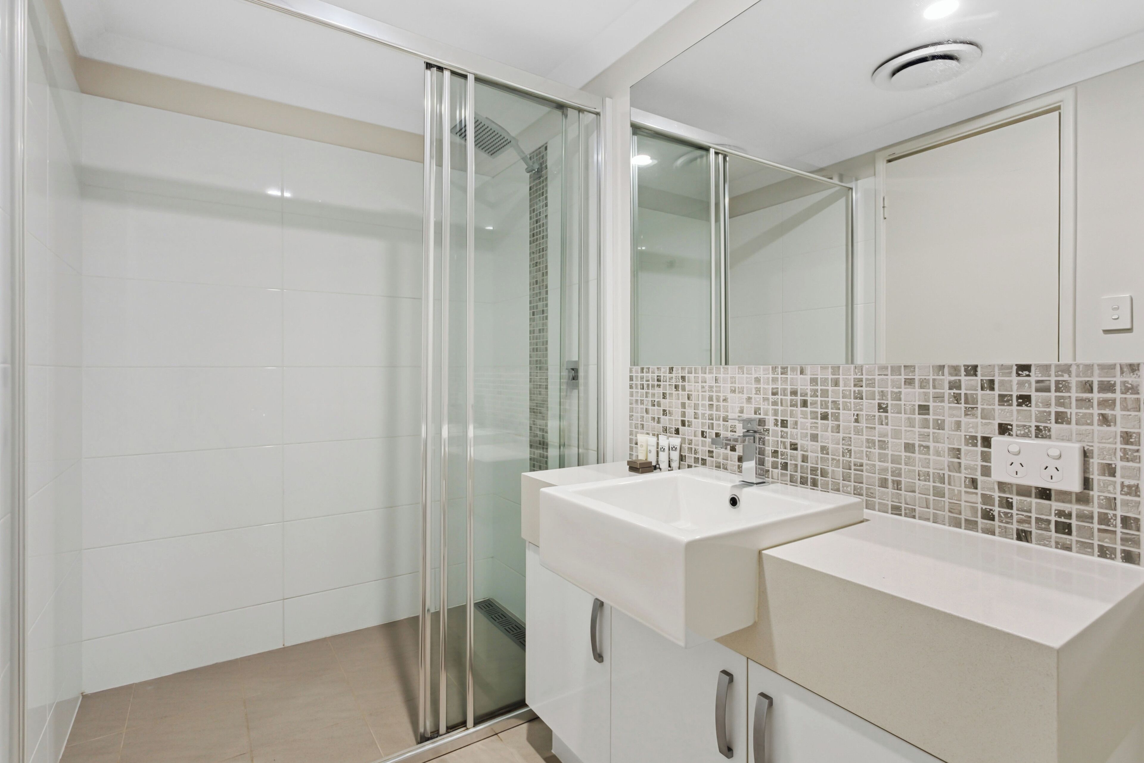 A modern bathroom with a glass shower enclosure, a white sink, and a tiled backsplash.
