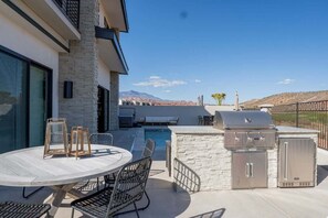Un patio exterior con una mesa redonda y sillas, una parrilla empotrada y una piscina.