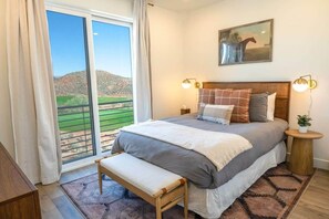 Une chambre à coucher avec un grand lit, un banc, une table de chevet avec une lampe et un tableau au mur.